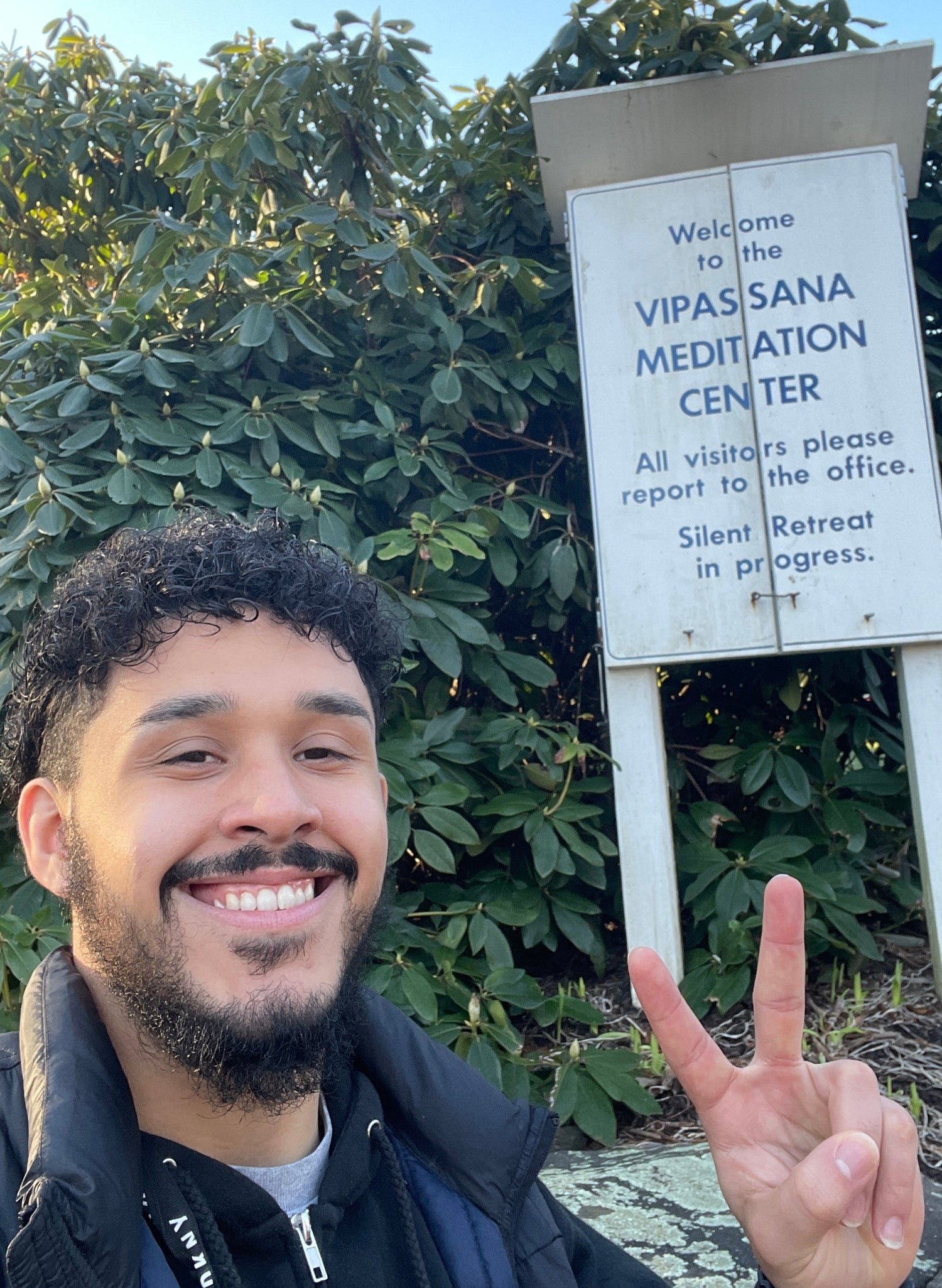 Person making a peace sign in front of a meditation center sign