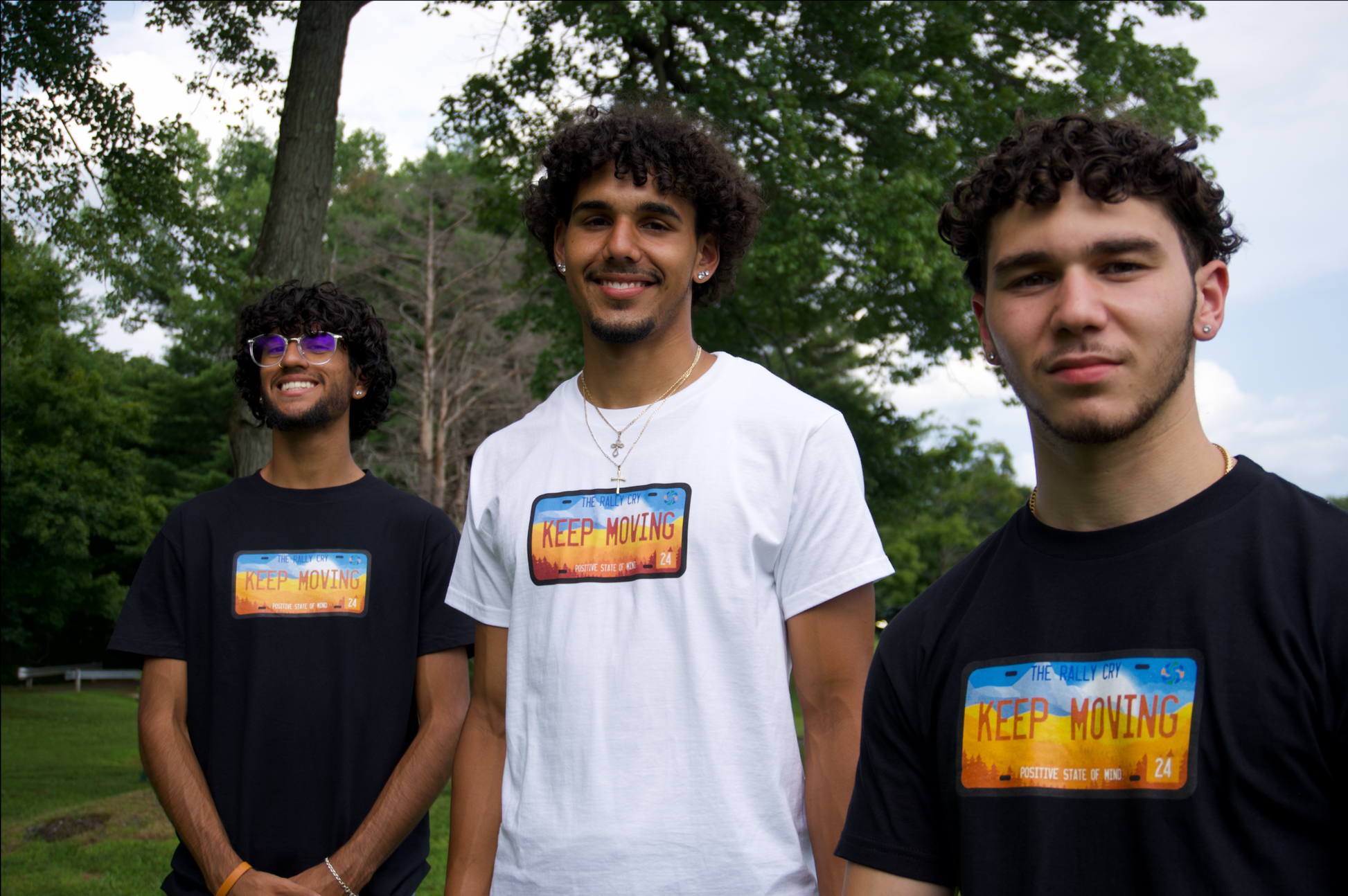 3 men wearing keep moving tees smiling, one is wearing white with others wearing black. 